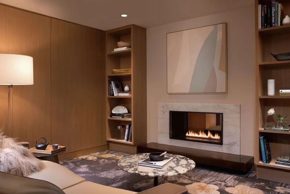 Sitzbereich einer Suite mit Kamin, Marmortisch, Regal und modernem Wandbild.