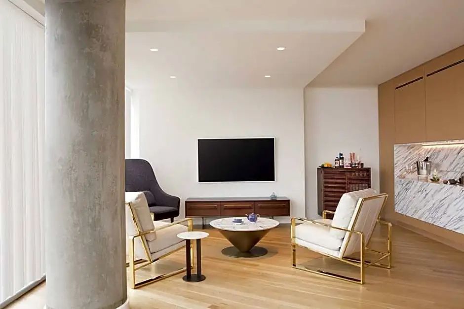Wohnzimmer einer Suite mit zwei Sesseln, Marmortisch, Flachbild-TV und Holzboden.