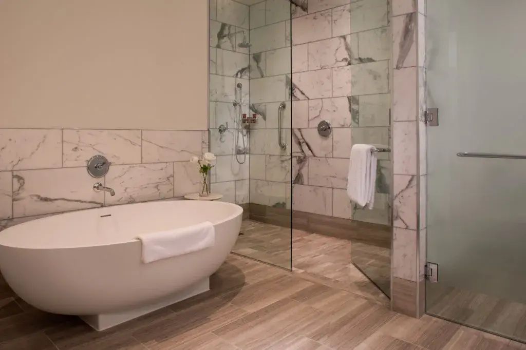 Badezimmer mit freistehender Badewanne, bodengleicher Glasdusche und Marmorwänden.