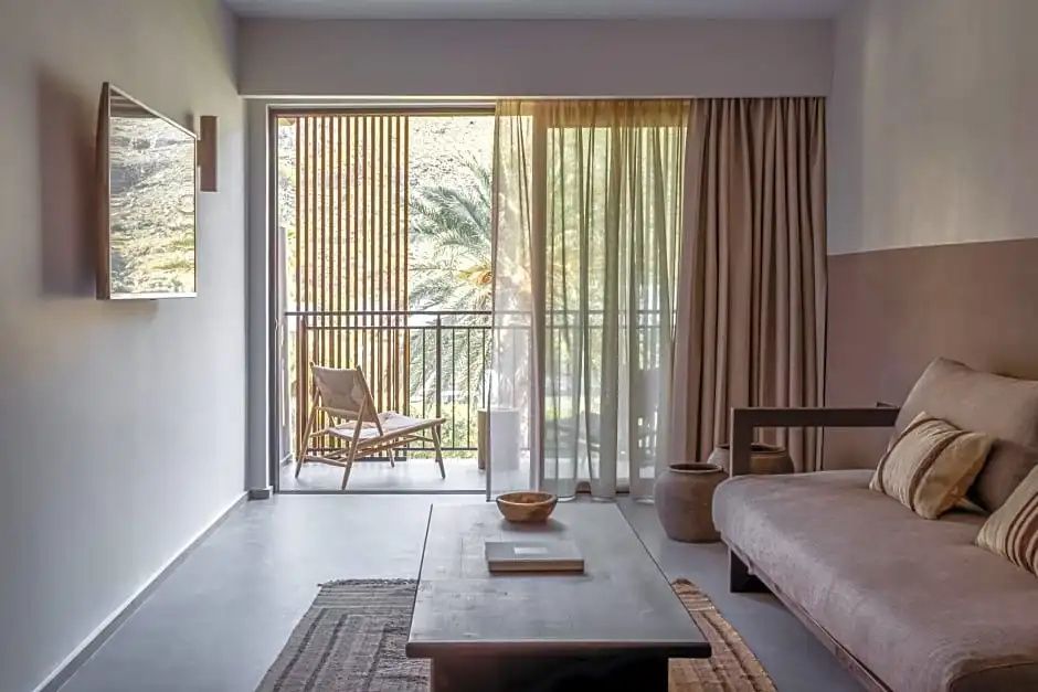Sitzbereich im Hotelzimmer mit Holztisch und Blick auf den sonnigen Balkon.