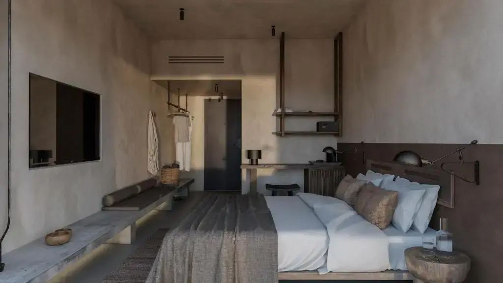 Ansicht eines Hotelzimmers mit Doppelbett, Holzregal, Schreibtisch und Sitzbank.