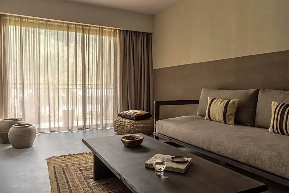 Wohnbereich eines Hotelzimmers mit Couch, hölzernem Couchtisch und großem Fenster.