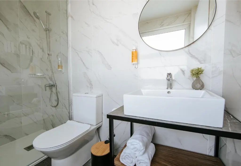 Modernes Badezimmer in Marmoroptik mit eckigem Waschbecken, rundem Spiegel und Dusche.