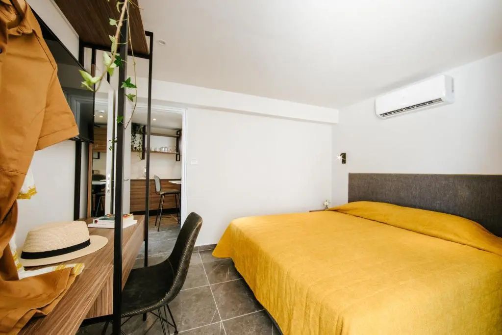 Schlafbereich im Hotelzimmer mit einem Bett mit gelber Tagesdecke sowie Schreibtisch und Stuhl.