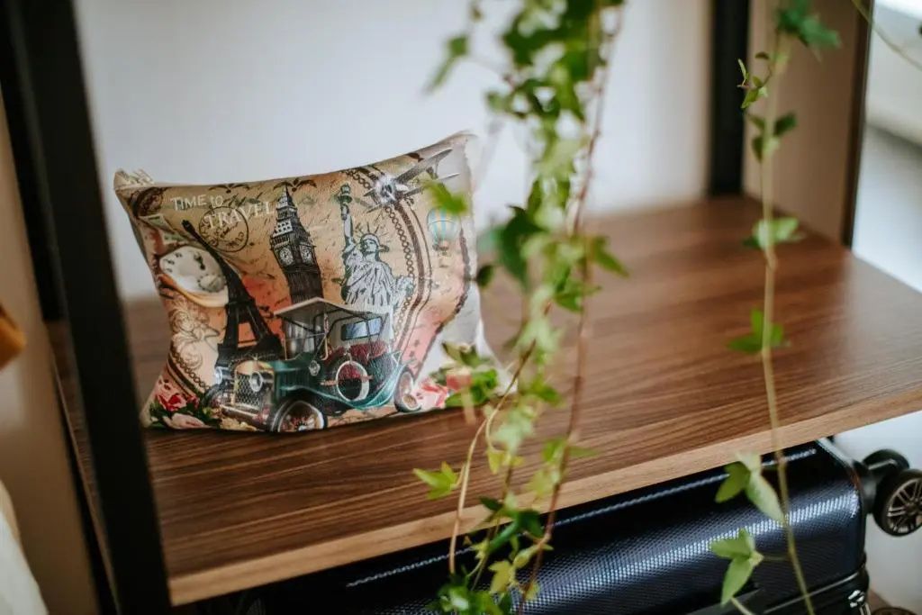 Ein Dekokissen mit Reisemotiven liegt auf einer Holzablage neben Efeuranken.