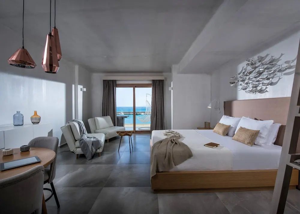 Schlafbereich einer Suite mit Doppelbett, Sitzgelegenheiten und Fensterfront zum Meer.