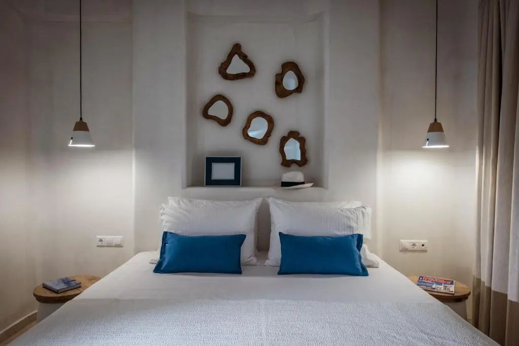 Doppelbett mit weißer Bettwäsche, blauen Kissen und dekorativen Wandspiegeln in Holzrahmen.