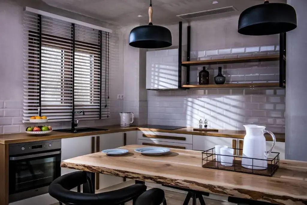Offene Küche mit Holz-Esstisch, schwarzen Stühlen, weißem Fliesenspiegel und Regalen.
