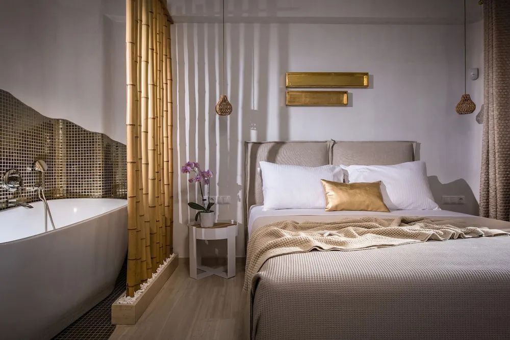 Helles Schlafzimmer mit beige gedecktem Doppelbett und Bambustrennwand zum angrenzenden Badbereich.