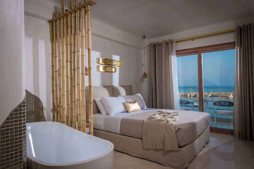 Schlafzimmer mit Doppelbett, Raumteiler aus Bambus, Badewanne und Balkontür mit Meerblick.