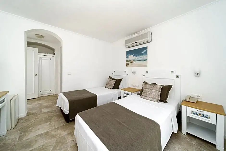 Zwei Einzelbetten in einem weiß gestrichenen Hotelzimmer mit Fliesenboden.
