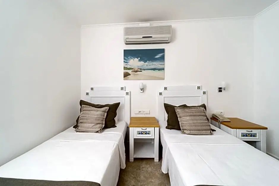 Zweibettzimmer mit weißen Betten, Kissen, einem Nachttisch und einer Klimaanlage an der Wand.