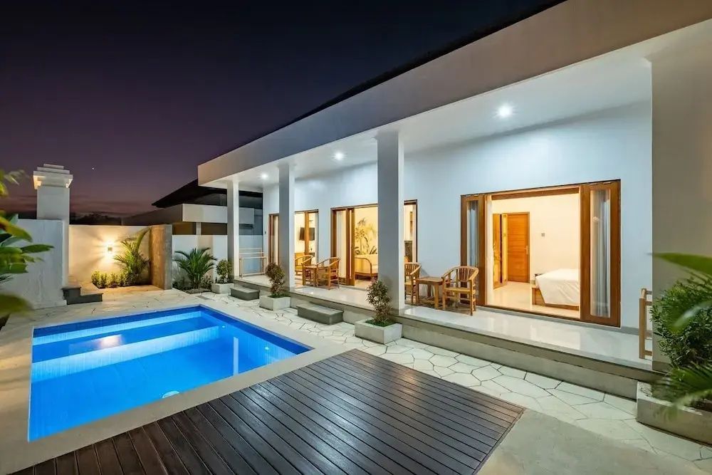 Beleuchtete Villa mit überdachter Terrasse und integriertem Außenpool am Abend.