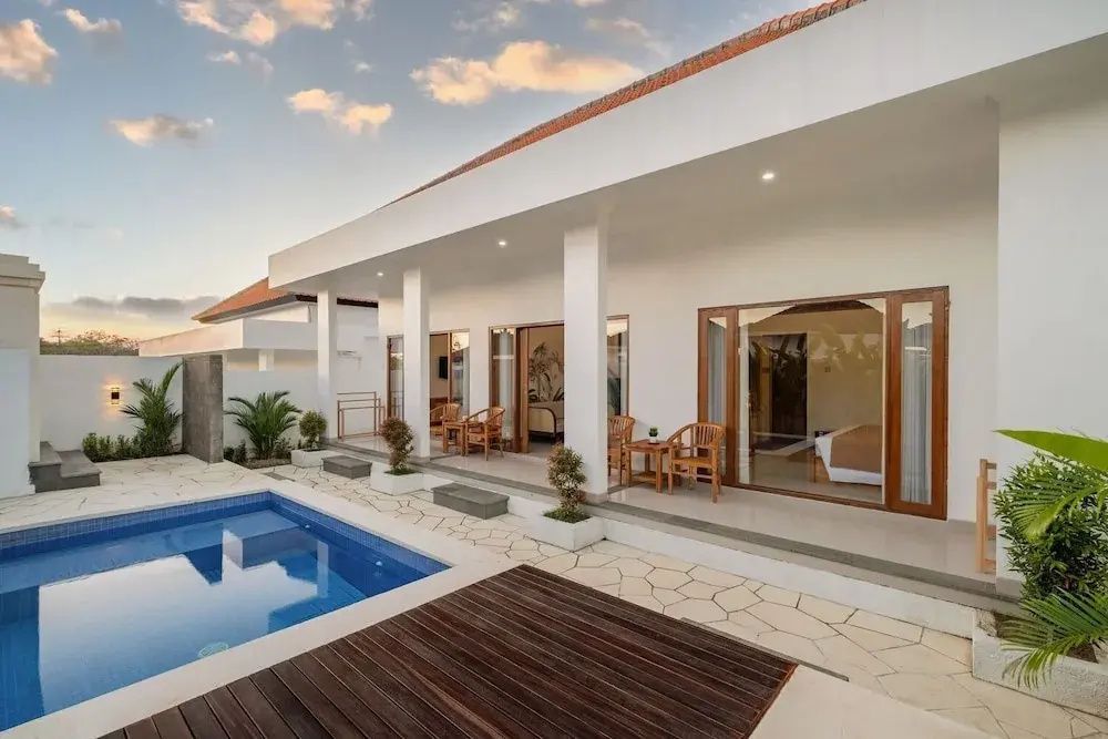 Weißer Bungalow mit Holzstühlen auf der Terrasse und einem blauen Pool.