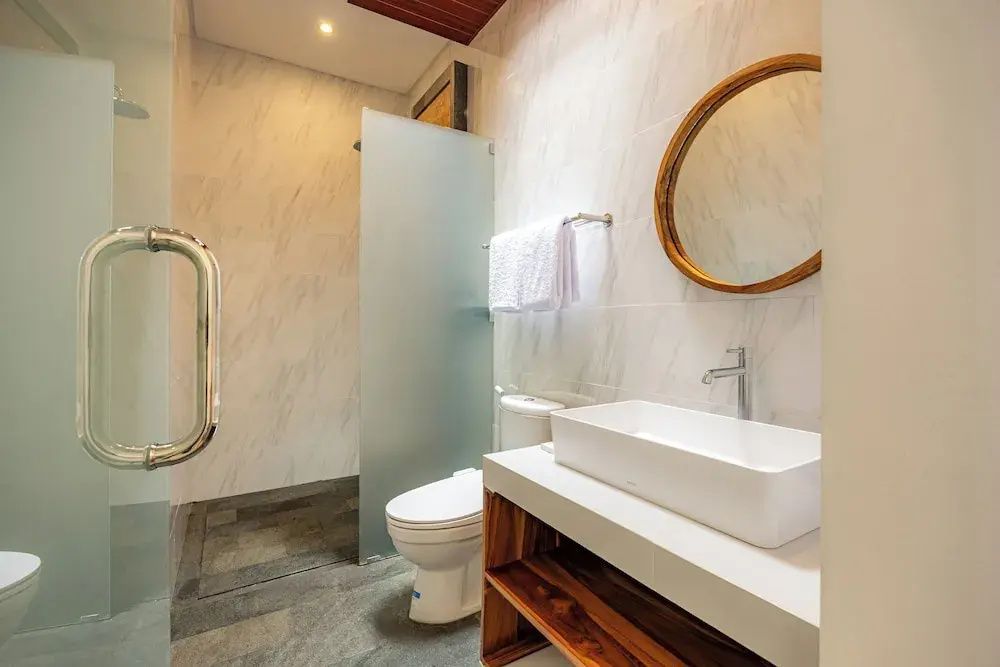 Badezimmer mit weißem Waschbecken auf Holztisch, rundem Spiegel und einer Toilette.