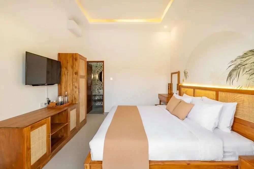 Hotelzimmer mit Holzdoppelbett, flachem Fernseher auf einem Schrank und Blick ins Bad.