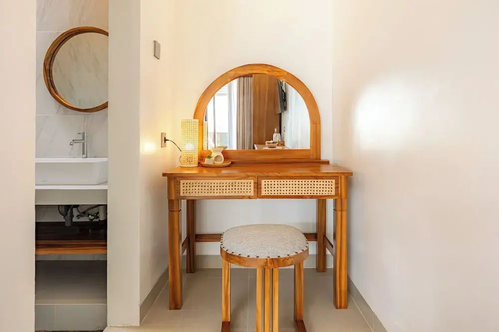 Holzschminktisch mit halbrundem Spiegel und passendem Hocker vor einer weißen Wand.