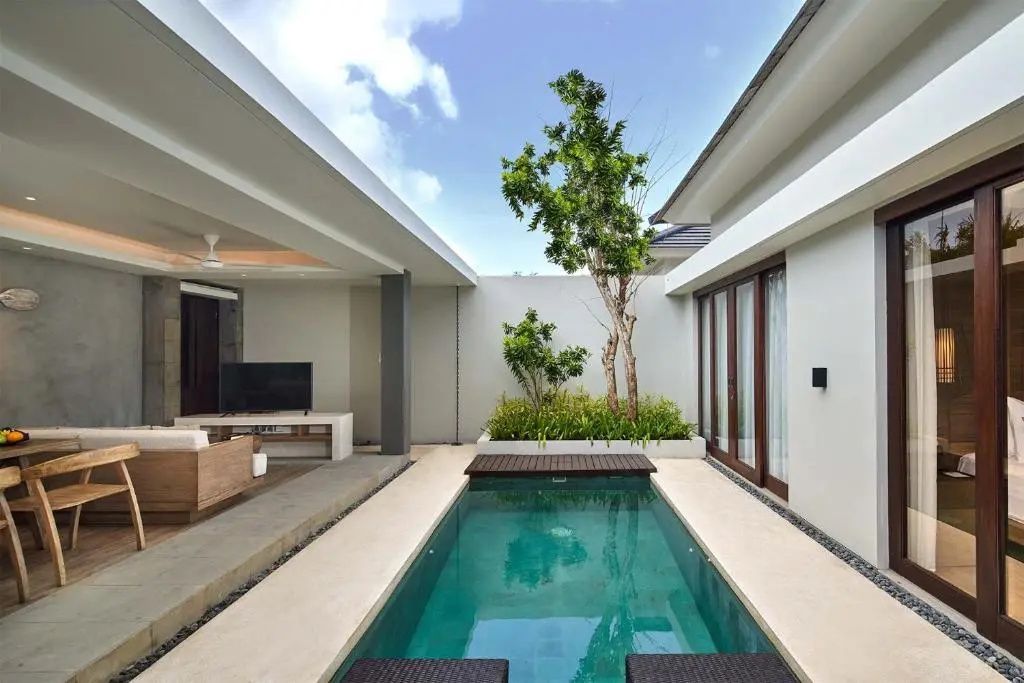 Innenhof einer Villa mit einem schmalen Pool, Terrasse und Bepflanzung unter blauem Himmel.