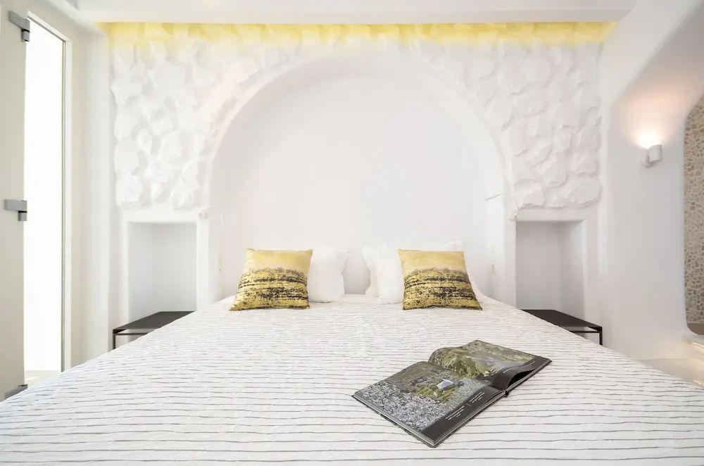 Doppelbett mit gelben Musterkissen, aufgeschlagenem Magazin und weißer Steinwand.