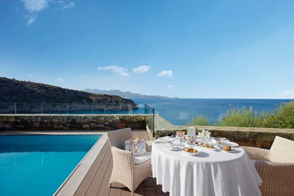 Sonnige Terrasse mit gedecktem Frühstückstisch, Pool und Blick auf das blaue Meer.
