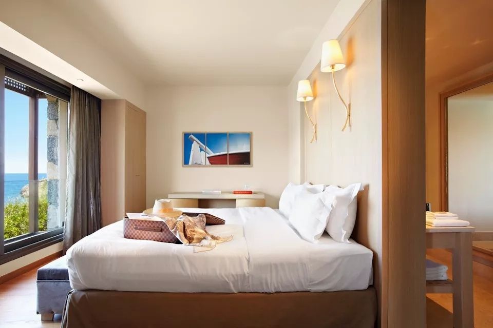 Helles Hotelzimmer mit bezogenem Doppelbett, zwei Wandleuchten und einem Bild an der Wand.