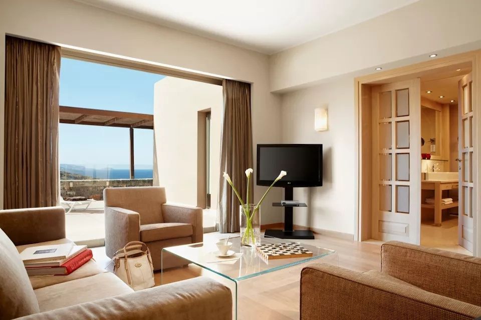 Wohnbereich einer Suite mit Sesseln, Glastisch und Zugang zur Terrasse mit Meerblick.