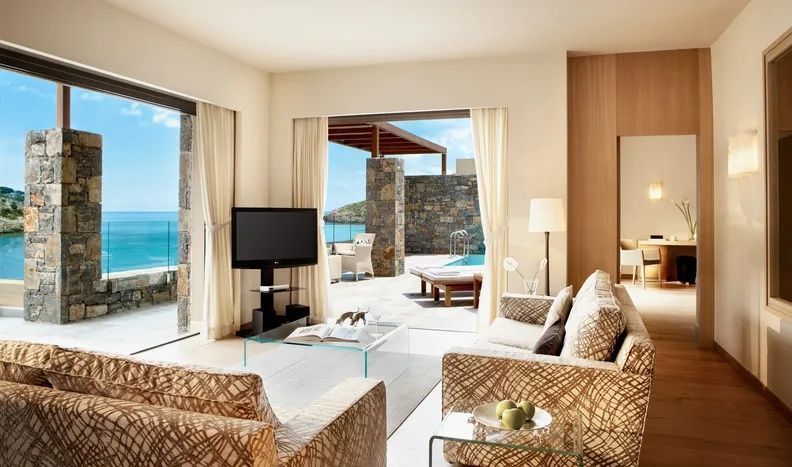 Wohnzimmer mit Sofa und großer Fenstertür zur Terrasse mit Privatpool und Meerblick.