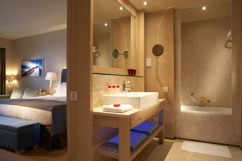 Badezimmer mit weißem Waschbecken, großem Spiegel und angrenzender Badewanne.