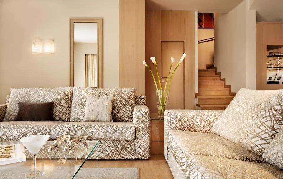 Wohnbereich mit gemusterten Sofas, Glastisch mit Blumen und einer Holztreppe im Hintergrund.