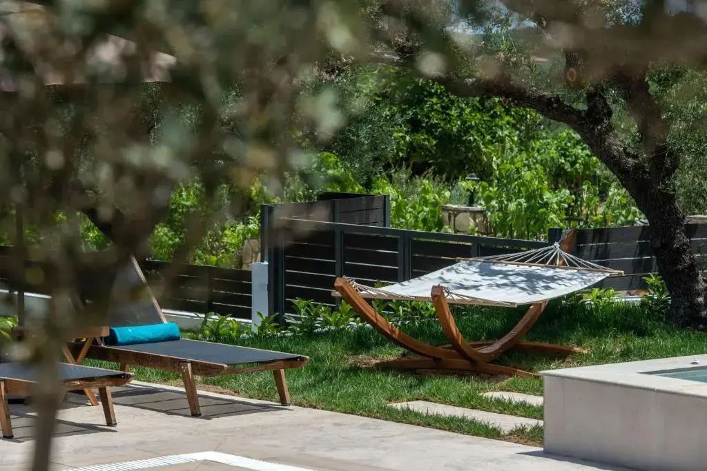 Gartenbereich mit einer Holzliege, einer Hängematte und schattenspendenden Bäumen.