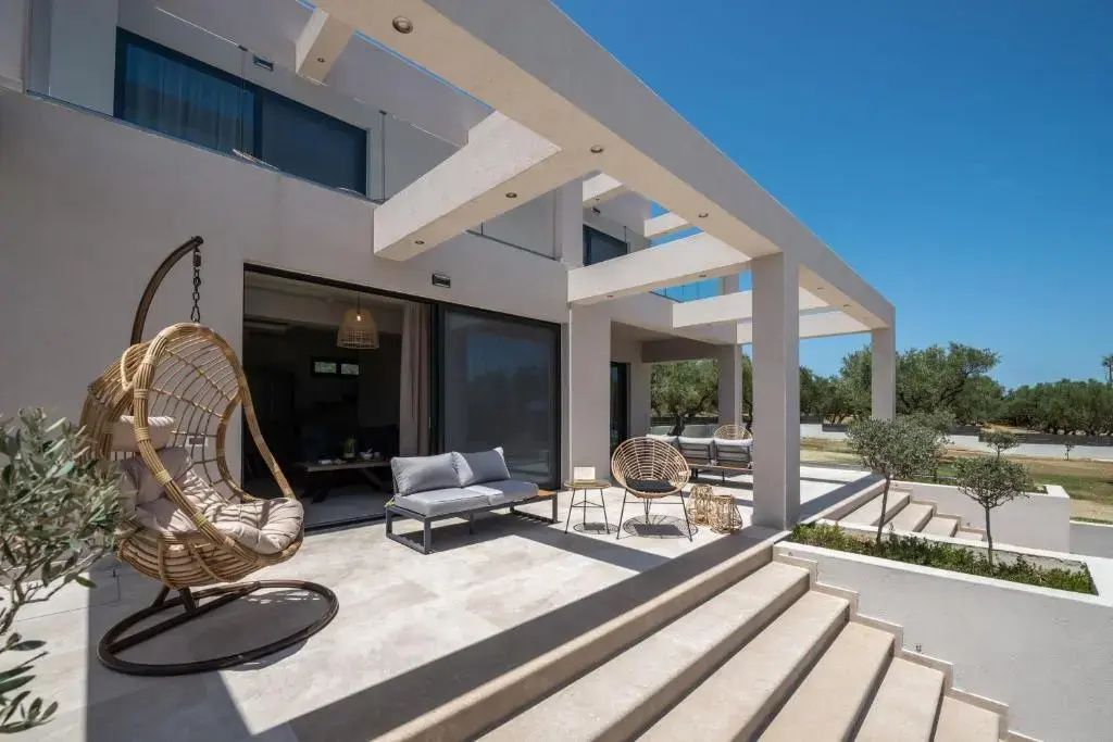 Sonnige Terrasse einer modernen Villa mit Sitzmöbeln, Hängesessel und Blick auf das Gebäude.