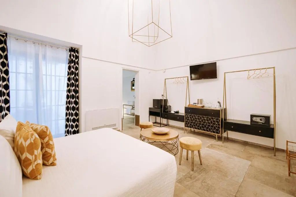 Helles Hotelzimmer mit weißem Bett, hölzernen Beistelltischen und Fernseher an der Wand.