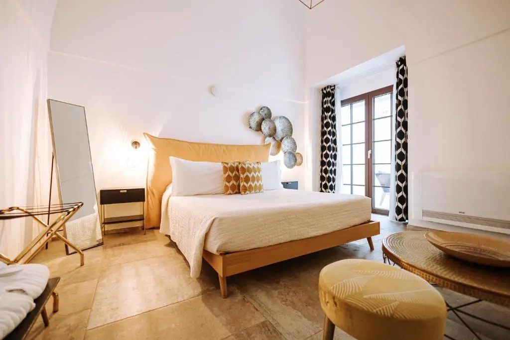 Geräumiges Hotelzimmer mit Doppelbett, Sitzecke und Balkontür mit Vorhängen.