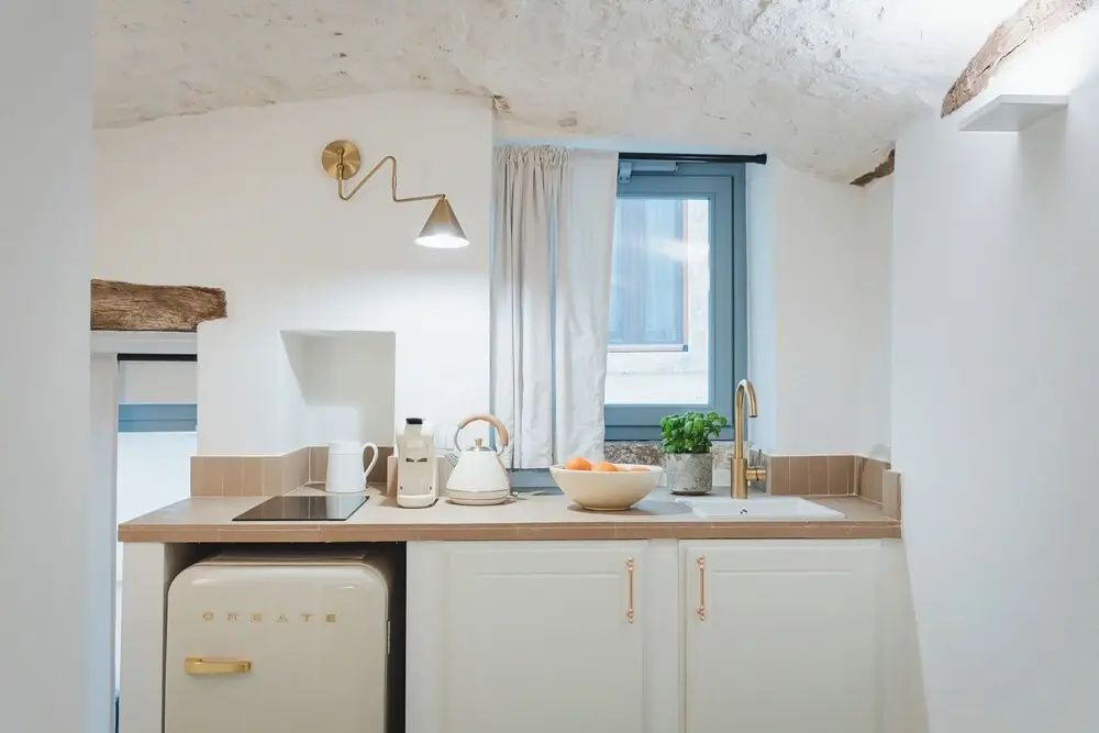 Kleine Küchenzeile mit Kochfeld, Spüle, Wasserkocher und Mini-Kühlschrank.