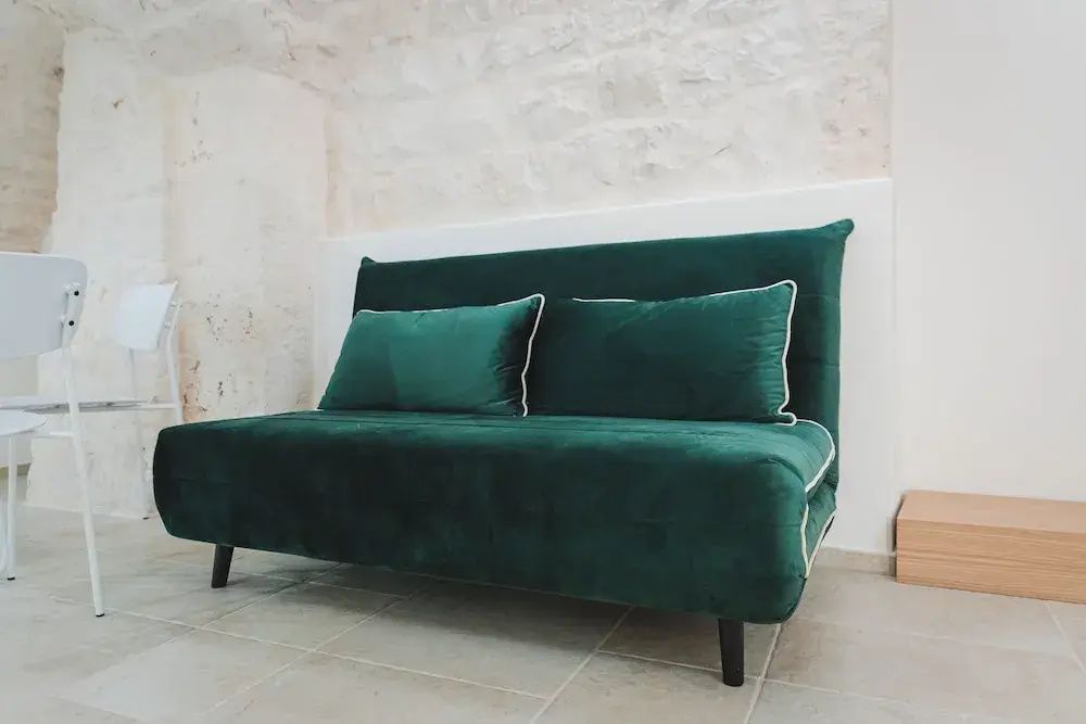 Grünes Samtsofa mit Kissen vor einer hellen Steinwand im Wohnbereich.