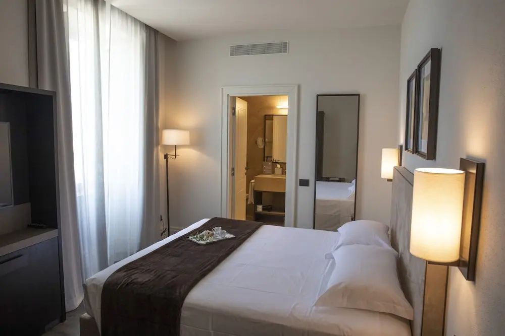 Helles Schlafzimmer mit braunem Bettläufer und Blick in das angrenzende Badezimmer.