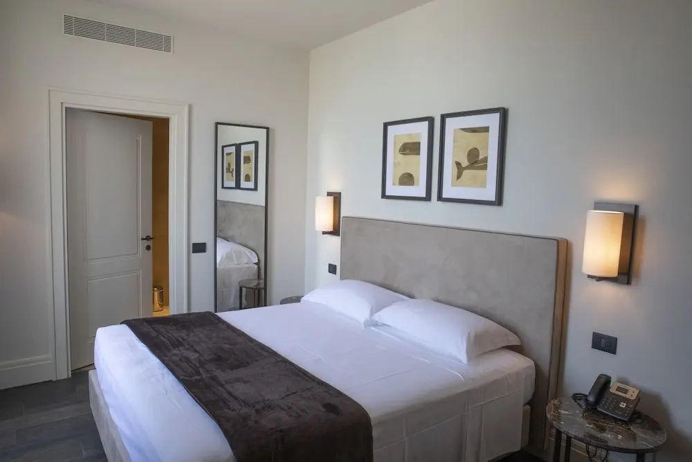 Doppelbett im Hotelzimmer mit zwei Bildern an der weißen Wand und großem Spiegel.