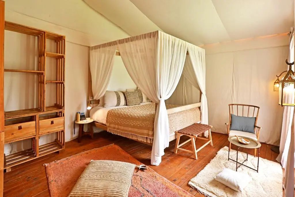 Helles Schlafzimmer im Zeltstil mit Holz-Himmelbett, Vorhängen und Holzfußboden.