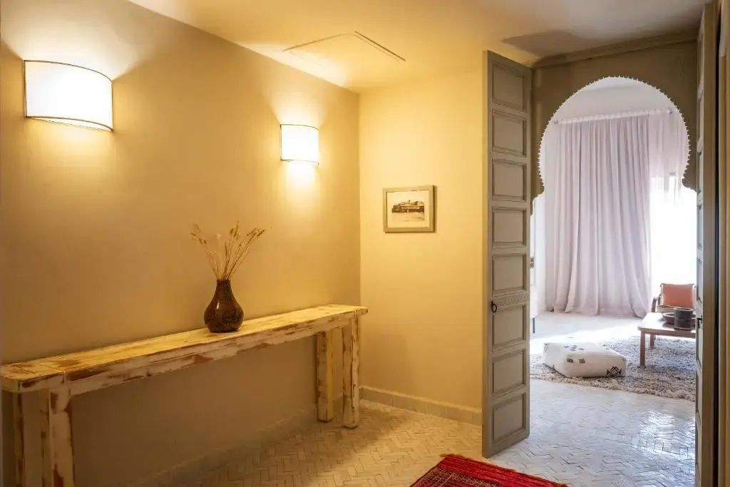 Heller Eingangsbereich einer Suite mit Holzkonsole, Wandleuchten und Durchgang zum Wohnraum.