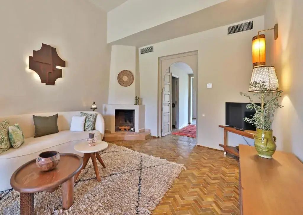 Wohnzimmer einer Suite mit Eckkamin, beigefarbenem Sofa, Teppich, Fernseher und Rundbogen-Durchgang.