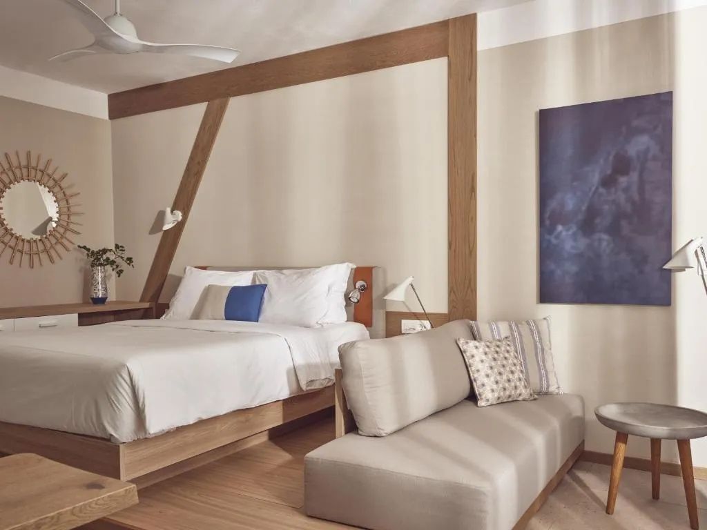 Modern eingerichtetes Hotelzimmer mit Doppelbett, hellem Sofa und Holzelementen an der Wand.