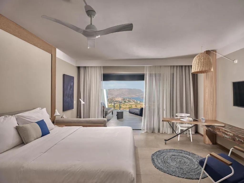 Helles Hotelzimmer mit Doppelbett, Schreibtisch und Zugang zur Terrasse mit Meerblick.
