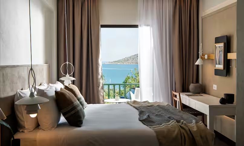 Blick vom Hotelbett durch die Balkontür auf das Meer und die Berge.