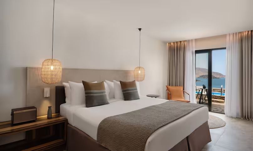 Modernes Doppelbett mit braun-grauen Kissen und Blick Richtung Balkon.