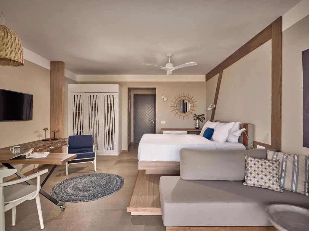 Helles Hotelzimmer mit Doppelbett, beigefarbenem Sofa, Schreibtisch und Kleiderschrank.