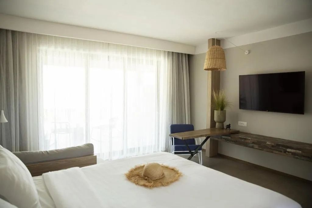 Doppelbett mit Strohhut im modern eingerichteten Hotelzimmer mit Schreibtisch.