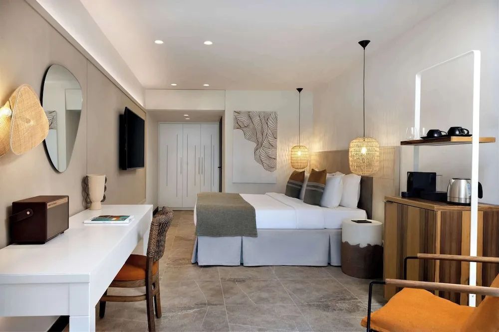 Geräumiges Hotelzimmer mit Schreibtisch, Wand TV und Doppelbett in warmen Tönen.