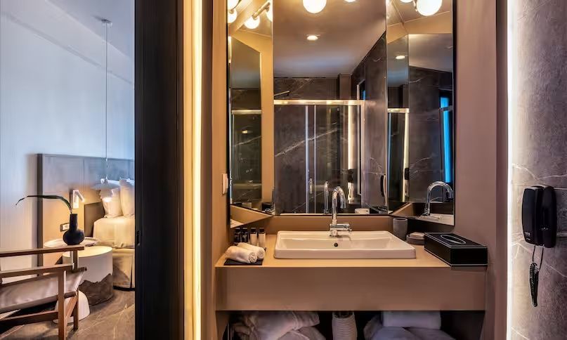Badezimmer mit beleuchtetem Spiegel, großem Waschtisch und Pflegemitteln.