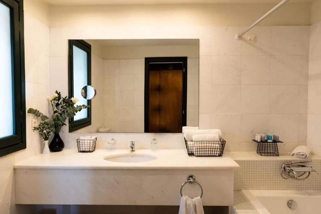 Badezimmer mit hellem Waschtisch aus Marmor, einem großen Spiegel und Handtüchern.