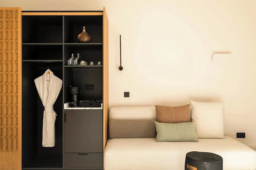 Offener Schrank mit Bademantel und Kaffeemaschine neben einer hellen Couch.
